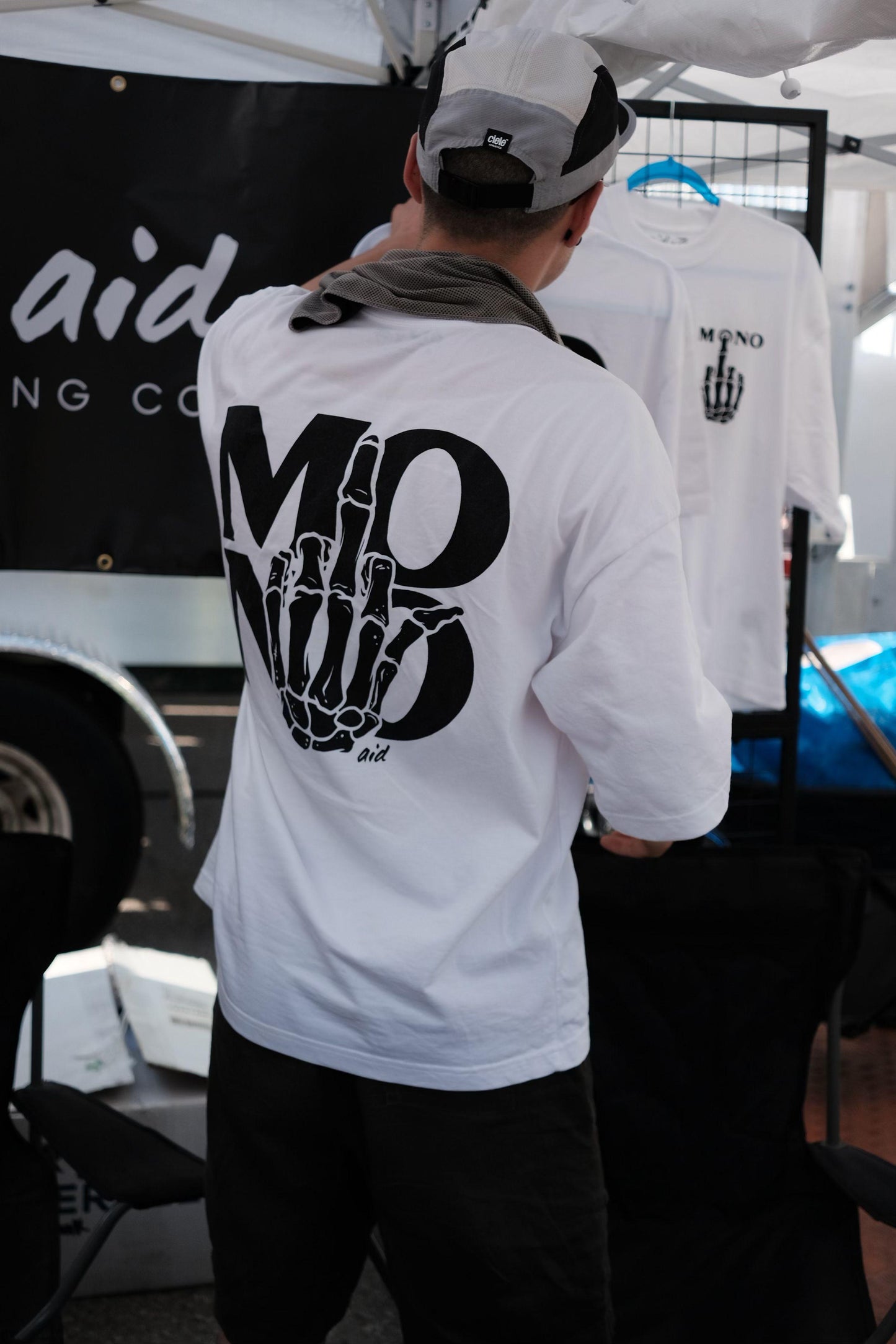 Person wearing a white tee with 'MONO' design, standing in front of a display with similar tees