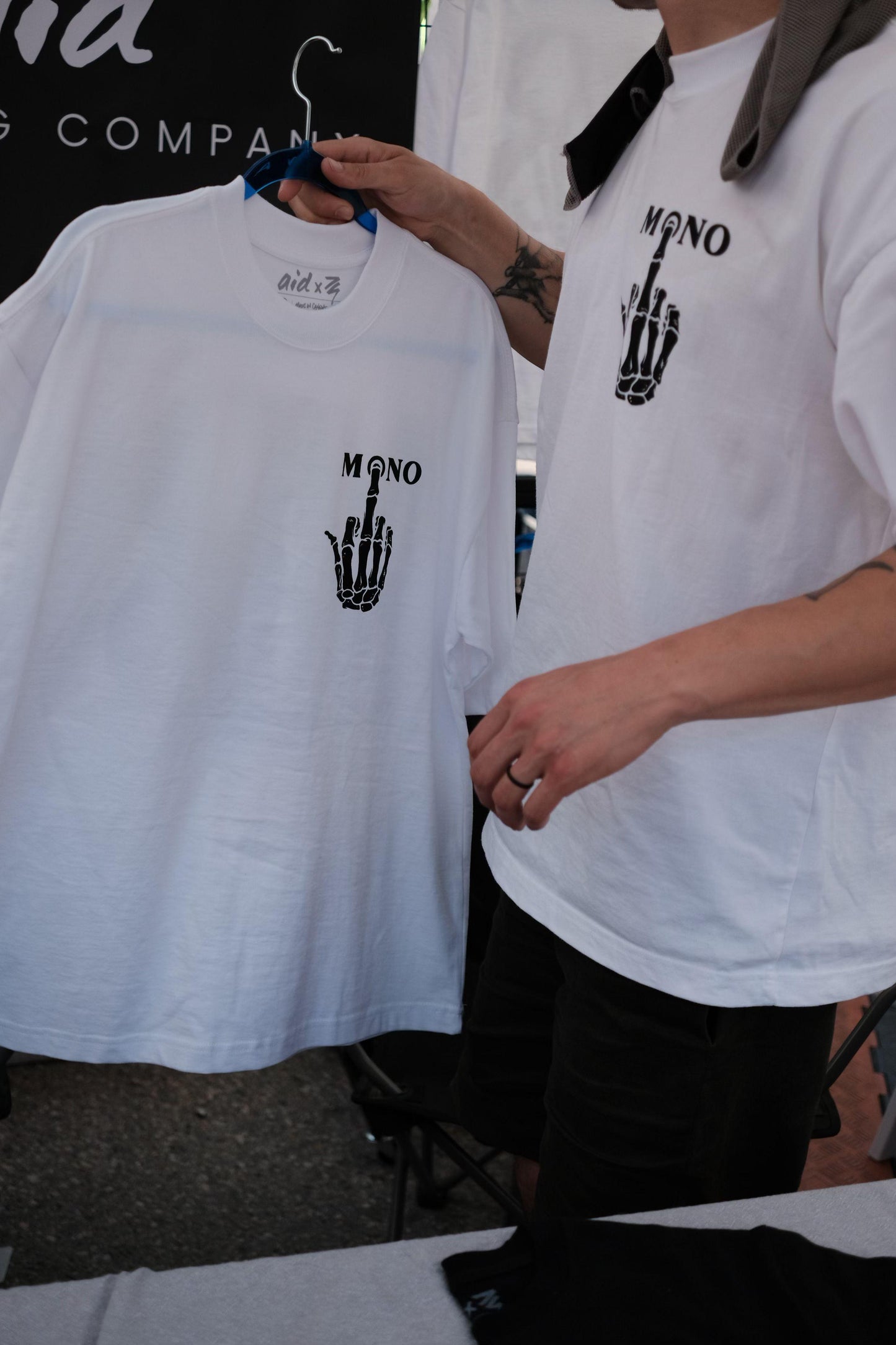Person holding a white t-shirt with 'MONO' design, wearing another white t-shirt with similar design.